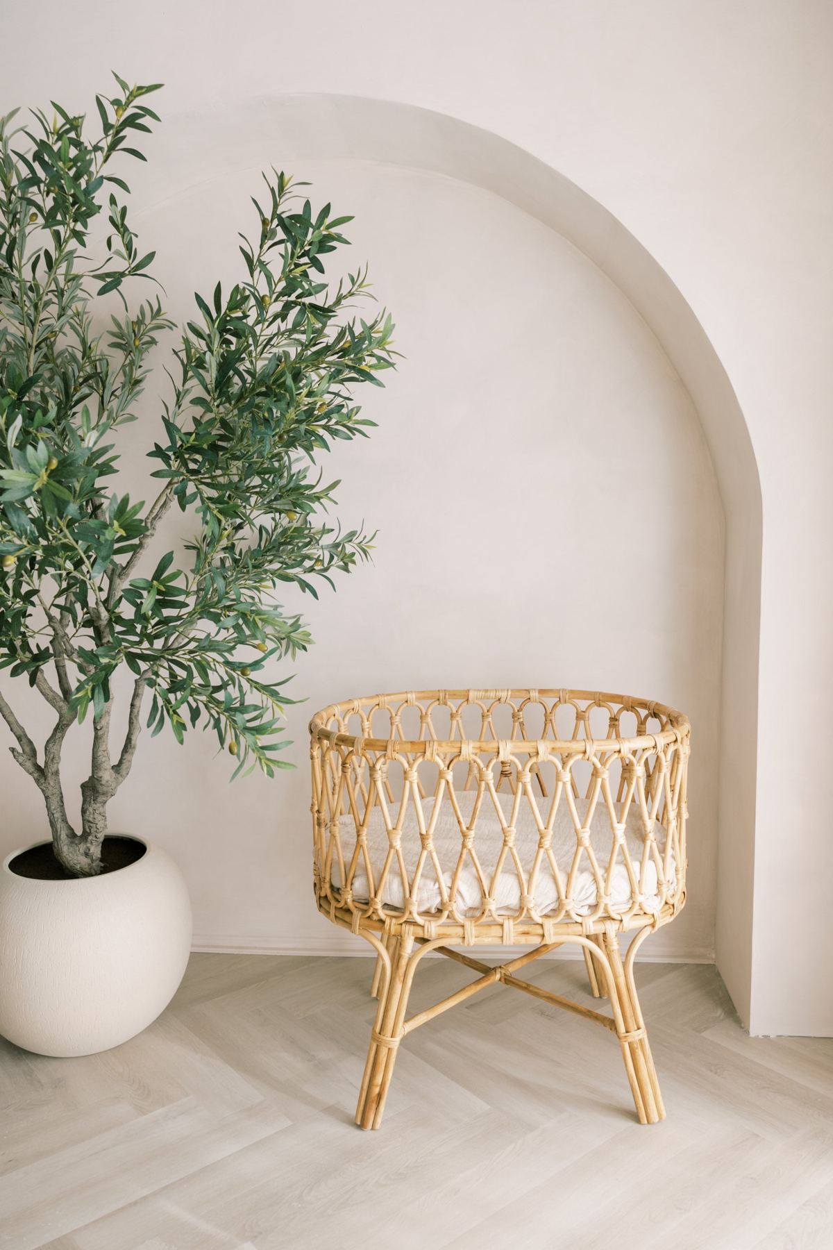 A woven rattan bassinet with soft bedding under the arch, beside the olive tree