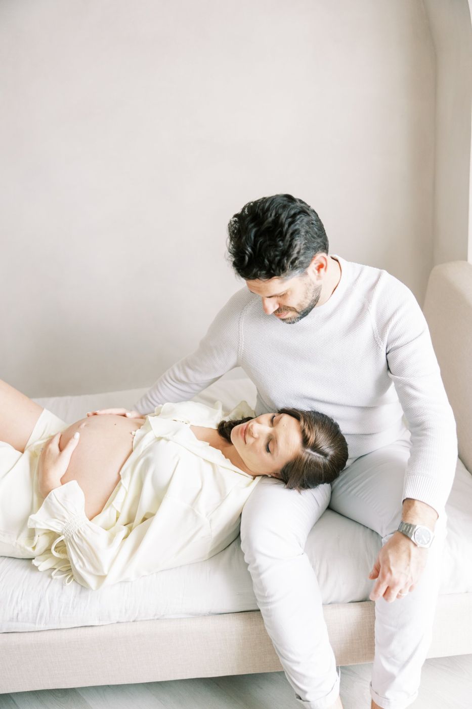 Expecting mother resting her head in her partner's lap on the daybed