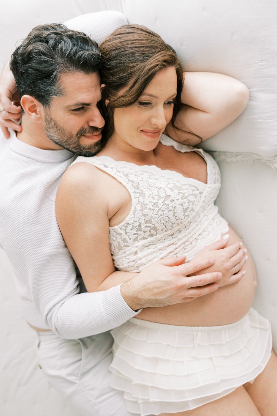Overhead view of an expecting couple cuddling on the white daybed