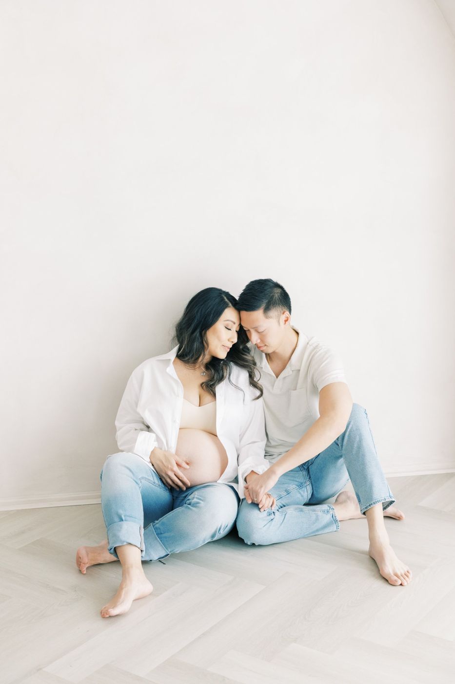 Expecting couple in jeans and white shirts sitting on the herringbone floor