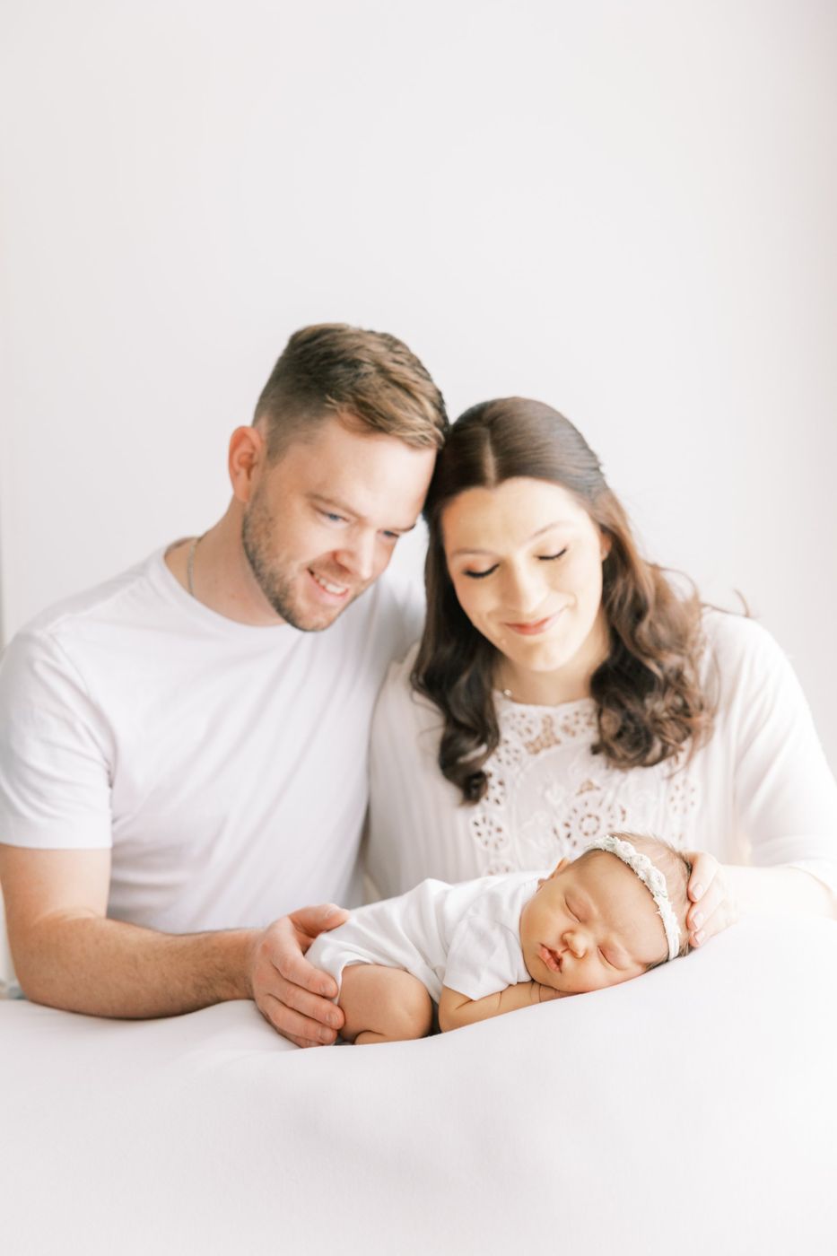 New parents smiling down at their sleeping newborn on a white blanket