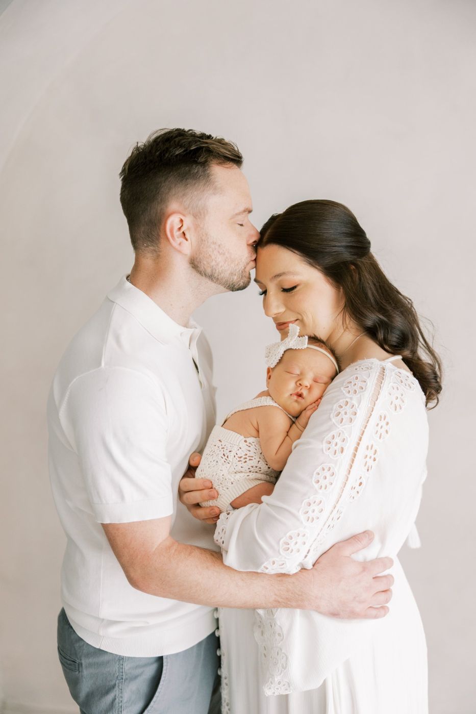 Father kissing mother's forehead as she holds their sleeping newborn