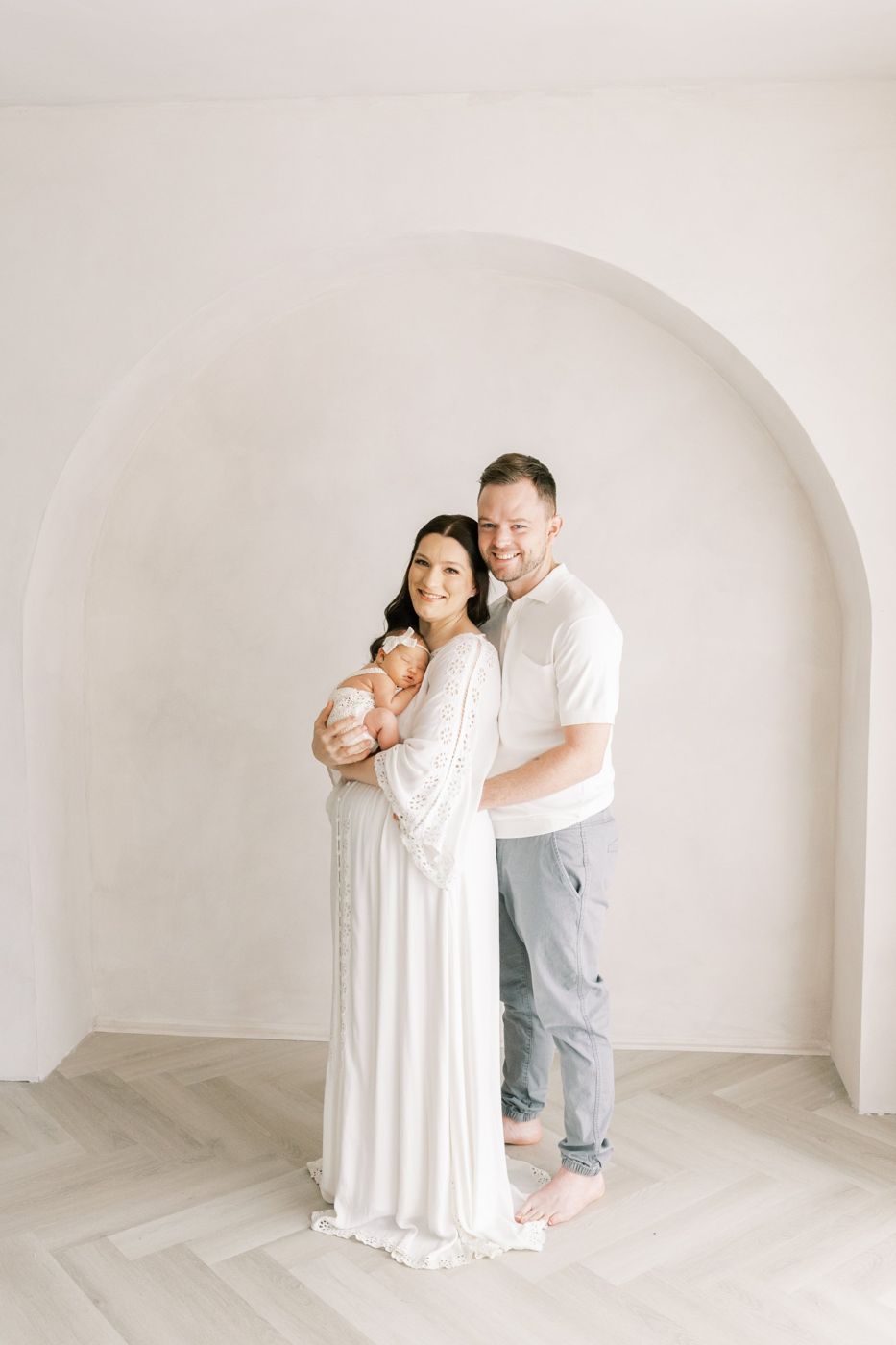 New parents holding their newborn under the limewashed arch