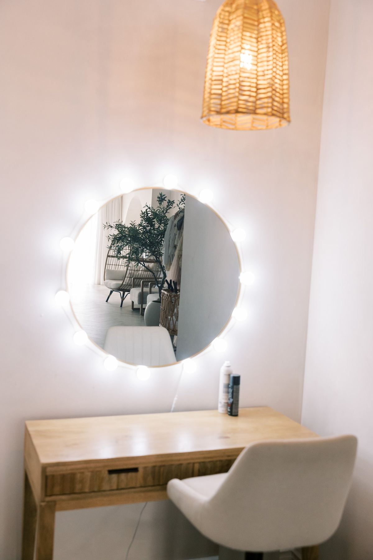 A wooden vanity with a round lit mirror and a white chair